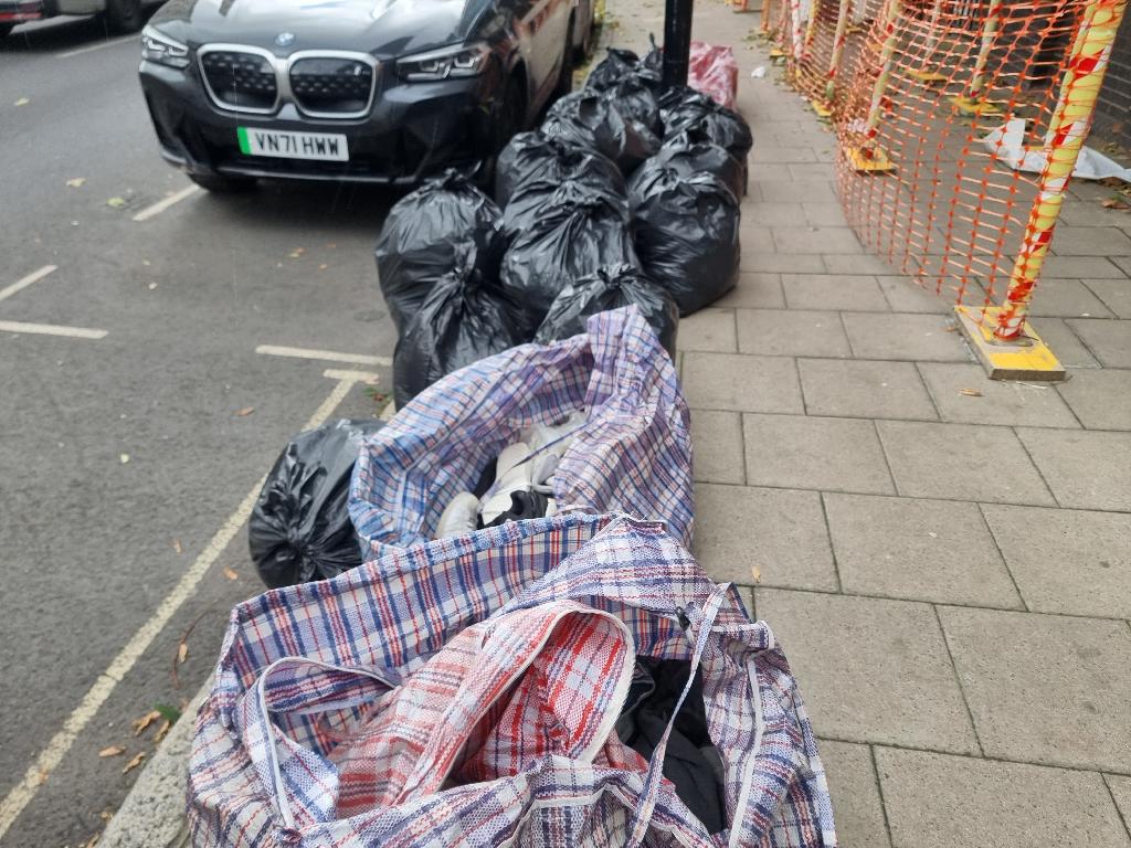 Before clothing and household item clearance in Bermondsey: bags of old clothing and footwear piled on the pavement near the curb