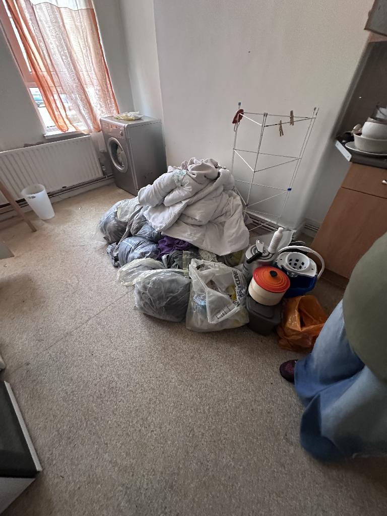 Flat clearance in Rotherhithe before the job, showing a corner filled with bundled laundry and stacked bags