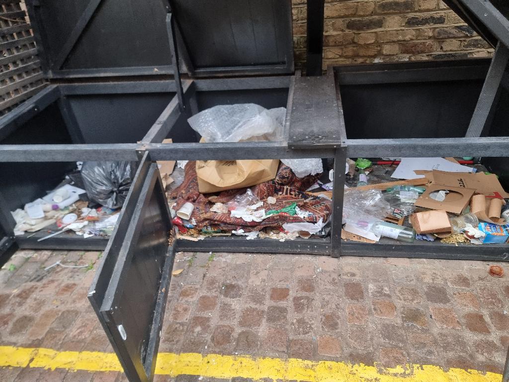 Before bin area clearance in Colville, showing mixed waste inside a metal bin bay and loose debris on the ground near the yellow line