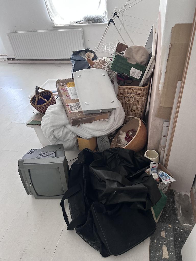 Flat clearance in Rotherhithe before the job, showing piled furniture items and textiles near a room corner