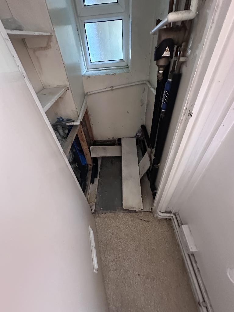 Flat clearance in Rotherhithe before the job, showing a cluttered corridor and stored items near pipework