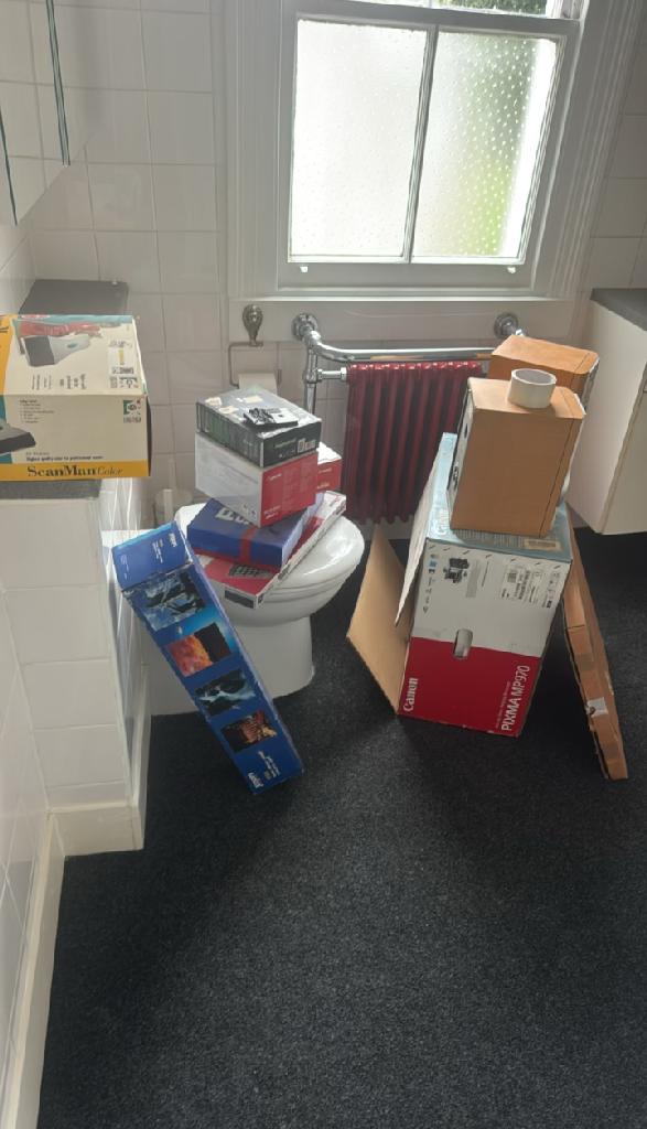 Flat clearance in Walham Green before the clearance, showing bathroom clutter with stacked cardboard boxes near the toilet