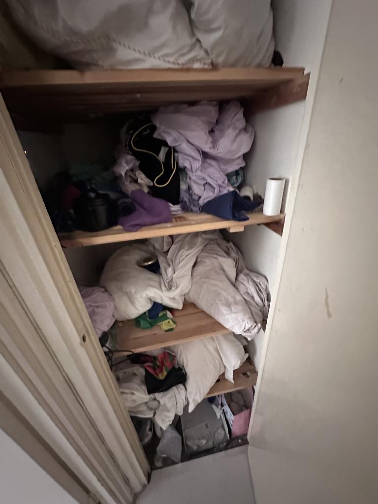 Flat clearance in Rotherhithe before the job, showing a cupboard shelf packed with textiles and household goods