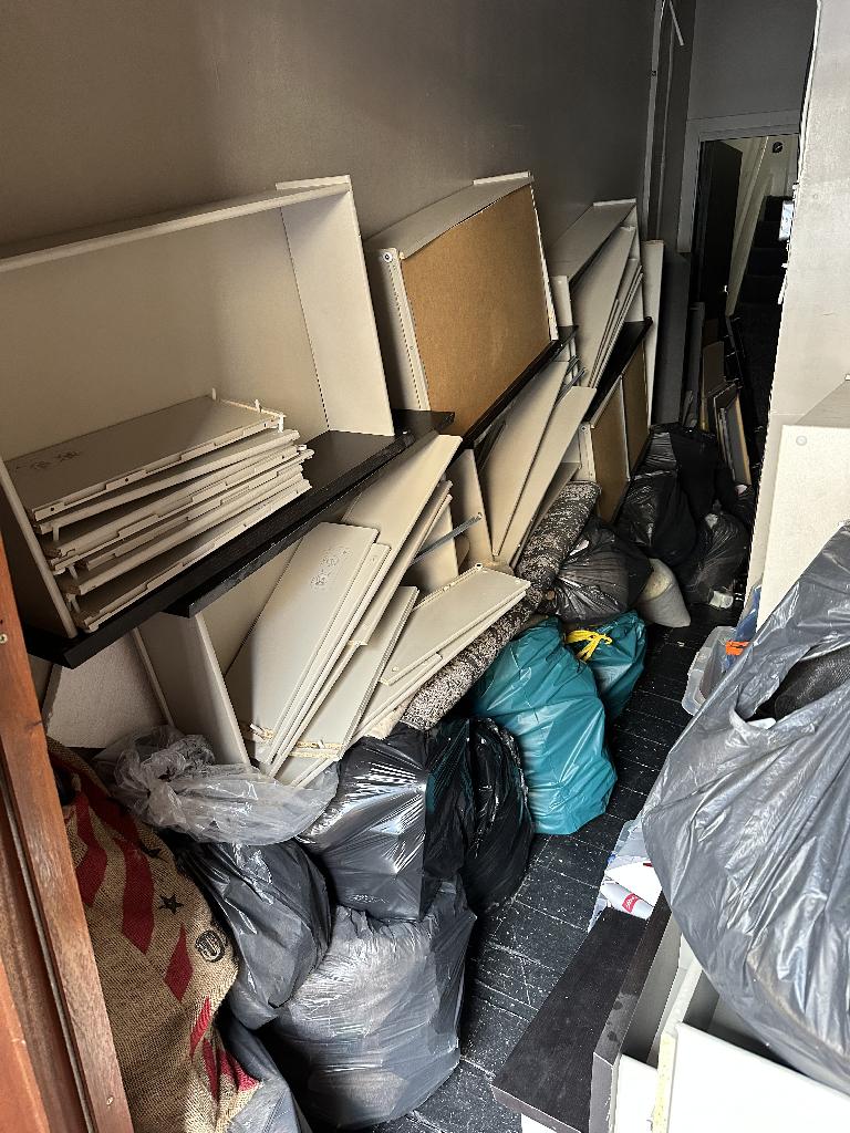 Internal household clearance in Clapham before service, showing mixed waste bags and panels stacked in a storage corner